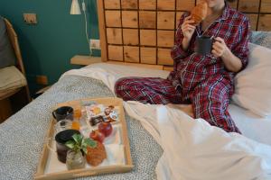 une femme assise sur un lit avec un plateau de nourriture dans l'établissement La Cordata Accommodation - Hotel Woodhouse, à Cinisello Balsamo