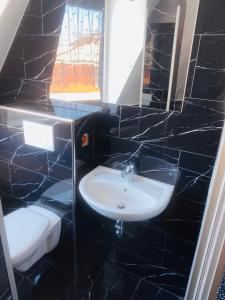 a black tiled bathroom with a sink and a toilet at Pic Pension in Warin