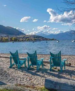 three green chairs sitting on a beach next to a lake at Top Floor on Okanagan Lake with AC & Heated Pool in Vernon