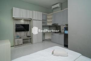 a kitchen with white cabinets and a tv and a bed at Yayah Rooms Bogor Syariah Mitra RedDoorz in Bogor