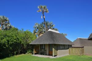 eine Hütte mit einem Strohdach und einer Palme im Hintergrund in der Unterkunft Palmwag Lodge in Palm