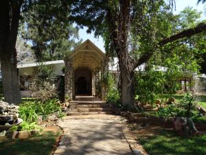 a stone house with a tree and a walkway at Kalahari Farmhouse Campsite in Stampriet