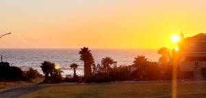 a sunset over the ocean with palm trees and a building at Jordan's Break in Jeffreys Bay