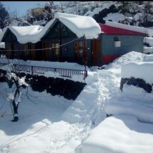 a house covered in snow next to a yard at Nandan Kanan Auli Resort in Joshīmath