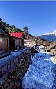 a house with snow on the ground next to a river at Nandan Kanan Auli Resort in Joshīmath
