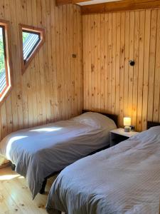 two beds in a wooden room with two windows at Cabañas Los Nevados in Nevados de Chillan