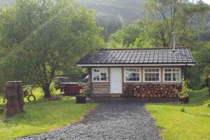 a small cabin in a yard with a stone wall at Pine Cabin, Strathyre. A cosy escape from it all. in Strathyre
