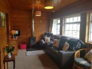 a living room with a leather couch and a stove at Pine Cabin, Strathyre. A cosy escape from it all. in Strathyre