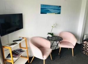 two pink chairs and a table and a tv at Blue Haven Motel in Mount Maunganui