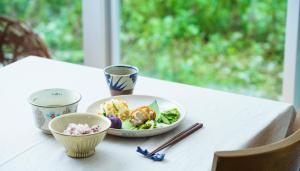 una mesa blanca con un tazón de comida y palillos chinos en Asahinoyado Shidakaji en Nanjo