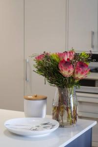 a vase of pink flowers and a plate on a counter at 9 Church View - No LoadShedding - Homely Apartment in Cape Town