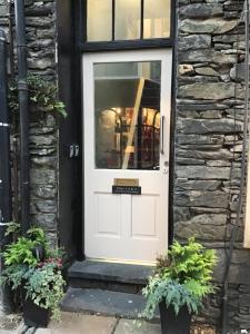 uma porta branca numa casa de pedra com dois vasos de plantas em No 3 Victoria Apartment em Bowness-on-Windermere