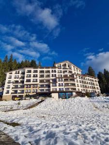 een groot wit appartementengebouw in de sneeuw bij Родопски Рай in Pamporovo
