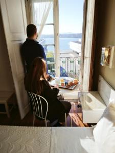 a man and woman sitting in a room looking out a window at Hotel Jardim Viana do Castelo in Viana do Castelo