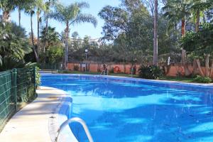 una gran piscina azul con una valla y palmeras en 3beds apartment Las Dunas walk to the beach, en Marbella