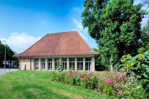 a building with a red roof and a garden with flowers at Taste Hotel Kulmbach in Kulmbach