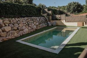 a swimming pool in a yard next to a stone wall at Collbato Resort. in Collbató