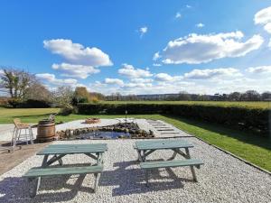 two picnic tables in front of a fire pit at Cosy Coppice Cottage in Whitchurch