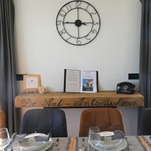 eine Uhr an einer Wand über einem Tisch mit Stühlen in der Unterkunft De Sint-Antoniushoeve in Zonnebeke