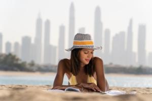 a woman sitting on a beach with a hat on at Th8 Palm Jumeirah, Accor in Dubai