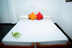 a white bed with four colorful pillows on it at Sunray Beach House in Tangalle