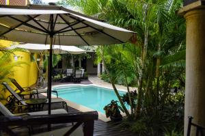 a swimming pool with an umbrella and chairs and a table at Hotel Marionetas in M&eacute;rida