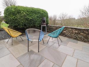 drie stoelen op een terras naast een stenen muur bij Coach House Cottage in Carnforth