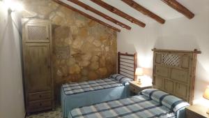 1 dormitorio con 2 camas y pared de piedra en Casas Rurales Cortijos el Encinar en Torres