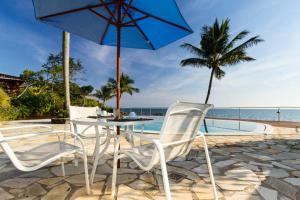 uma mesa e cadeiras com um guarda-sol e o oceano em Sol-lua Bangalo com uso exclusivo da piscina em Ilhabela