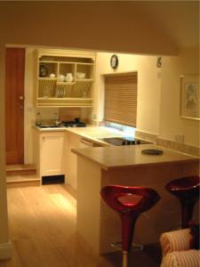 ペインズウィックにあるTibbiwell Lodgeの白いキャビネットとバースツール付きの島のあるキッチンが備わります。