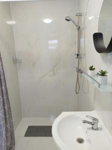 a white bathroom with a shower and a sink at Grafit Apartmanok in Hajdúnánás
