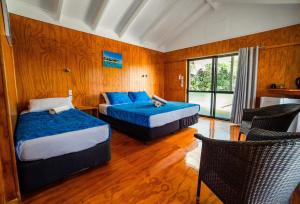 a bedroom with two beds with blue sheets and a window at Aitutaki Village in Arutanga