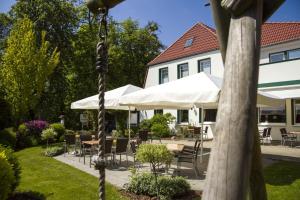 a patio with tables and chairs and white umbrellas at Landgasthof "Zum grünen Walde" in Nordholz