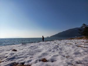 uma pessoa de pé em uma praia ao lado da água em 臨湖荘 em Takashima