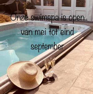 a hat and two glasses of wine next to a swimming pool at B&B De Joker in Turnhout