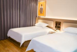duas camas num quarto de hotel com lençóis brancos em 银座佳驿（潍坊寒亭高铁北站店） em Weifang