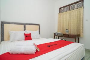 a bedroom with a bed with a red blanket and a desk at RedDoorz near Bundaran Ciceri in Kumprung