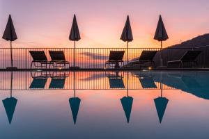 a pool with chairs and umbrellas in front of a sunset at Il Bagnolo Eco Lodge in Salò