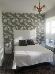 1 dormitorio con cama blanca y papel pintado con motivos florales en Vivienda de uso turístico Alma da Costa da Morte, en Sardiñeiro de Abajo