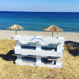 a white bench and two umbrellas on a beach at Sweet Kalimera Apartments in Kardamaina