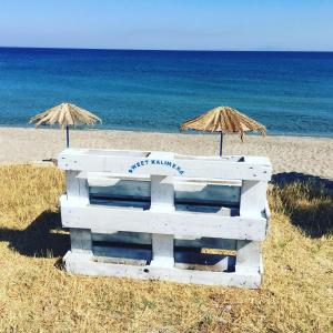 una panchina bianca e due ombrelloni su una spiaggia di Sweet Kalimera Apartments a Kardámaina