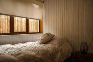Cama blanca en habitación con 2 ventanas en Refugio Simple Sur Casa 4 - 5 personas, en Malalcahuello