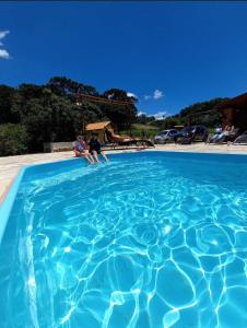 2 personnes assises dans une grande piscine bleue dans l'établissement Chácara Recanto dos Amores, à Bueno Brandão