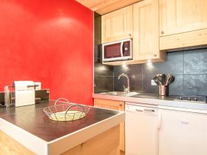 una cocina con armarios de madera y una pared roja en Studio Les Tommeuses - Val Claret-31 by Interhome, en Tignes