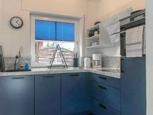 a kitchen with blue cabinets and a clock on a window at Holiday Home Sandmuschel by Interhome in Norddeich