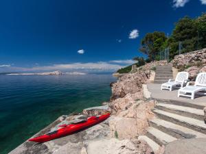 a red kayak sitting next to two white chairs and the water at Apartment Starigrad-4 by Interhome in Starigrad
