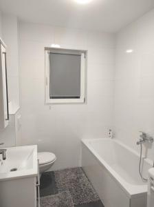 biała łazienka z wanną, toaletą i oknem w obiekcie Apartman MiMa w mieście Pale