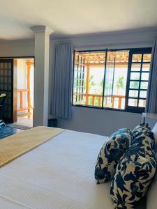 a bedroom with a bed with pillows and windows at Suíte frente mar e pés na areia in Japaratinga