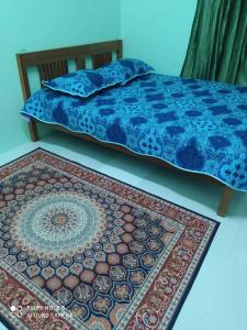 a bed with a blue comforter and a rug at Homestay AZMI ZITA in Kuala Terengganu
