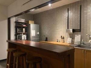 a kitchen with a counter with stools and a refrigerator at J-Hoppers Beppu Guesthouse ジェイホッパーズ別府ゲストハウス in Beppu